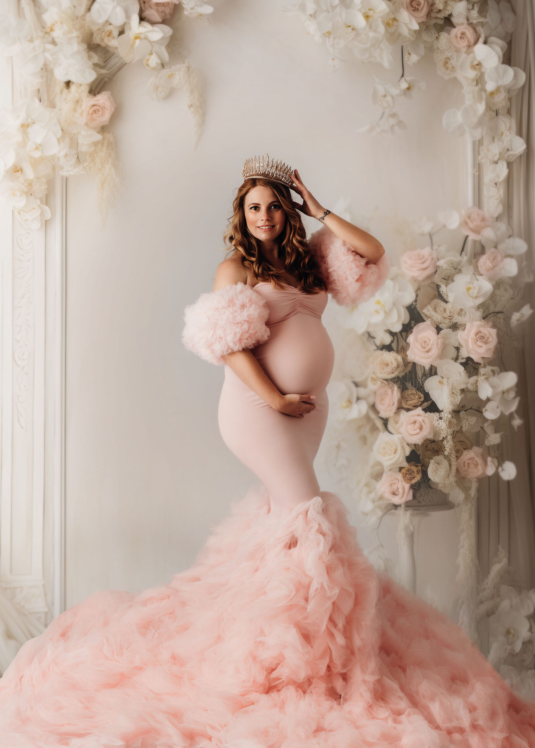 Schwangere Frau im langen Kleid in rosa mit der krone auf dem kopf