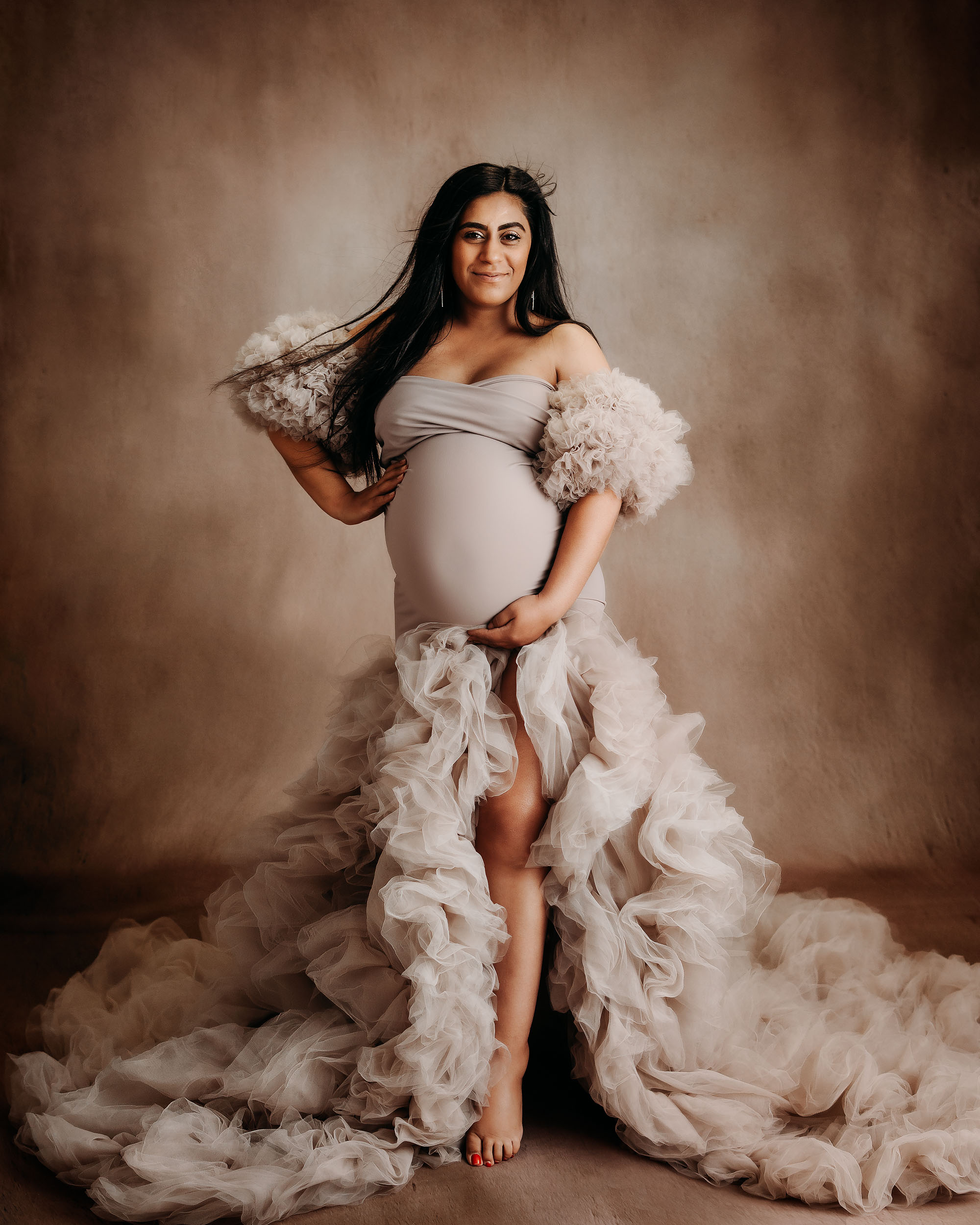 Elegant studio portrait of expectant mother in dramatic premium dress with soft lighting