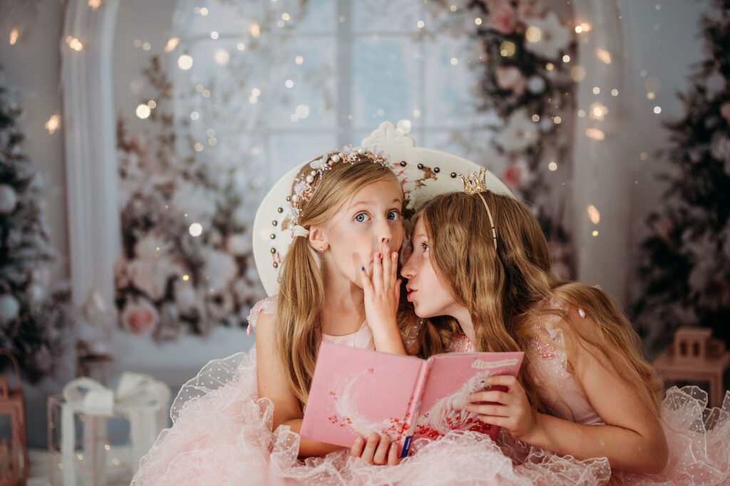Weihnachtsshooting Reutlingen Studio – zwei Mädchen in rosa Prinzessinnenkleidern im Gentle Pink Christmas Set, mit Teddybären, Weihnachtsbüchern, Lichterketten und festlicher Deko, elegante Fine-Art Familienfotografie