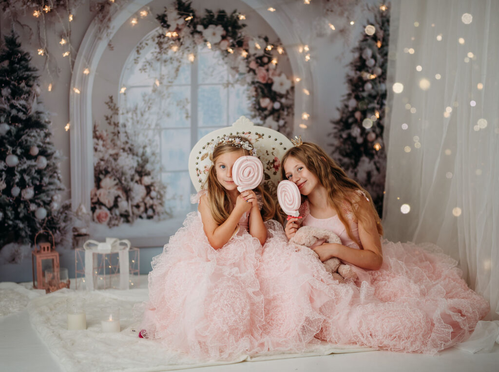 Weihnachtsshooting Reutlingen Studio – zwei Mädchen in rosa Prinzessinnenkleidern im Gentle Pink Christmas Set, mit Teddybären, Weihnachtsbüchern, Lichterketten und festlicher Deko, elegante Fine-Art Familienfotografie